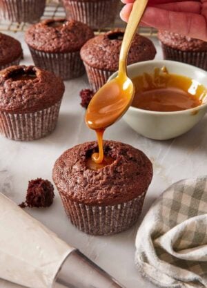 A chocolate cupcake being filled with caramel sauce, with more filled cupcakes in the background.