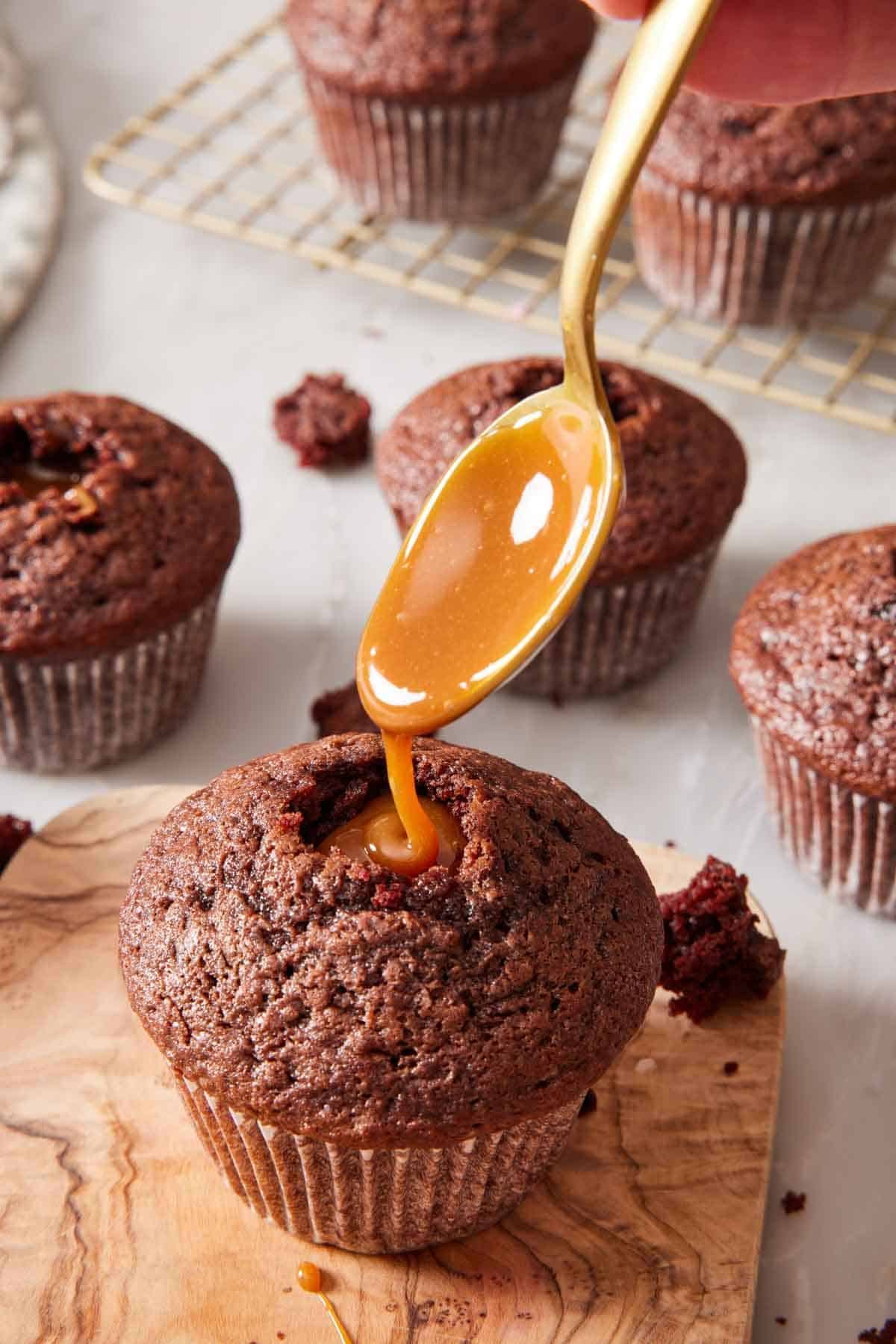 Chocolate cupcake being filled with caramel sauce. More filled cupcakes in the background.