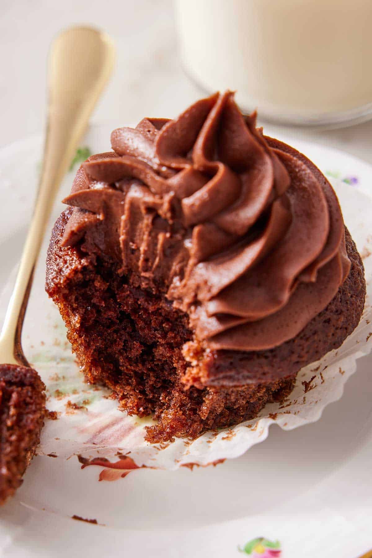 Close-up of a frosted chocolate cupcake with some scooped out on a fork.