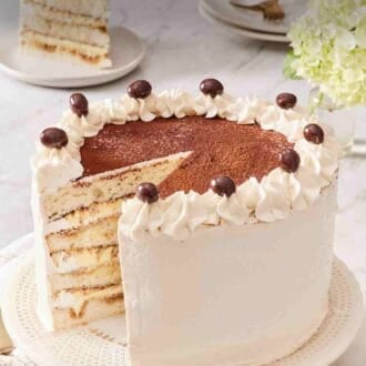 Pinterest graphic showing tiramisu cake on a cake stand with a slice removed and placed on a plate in the background.