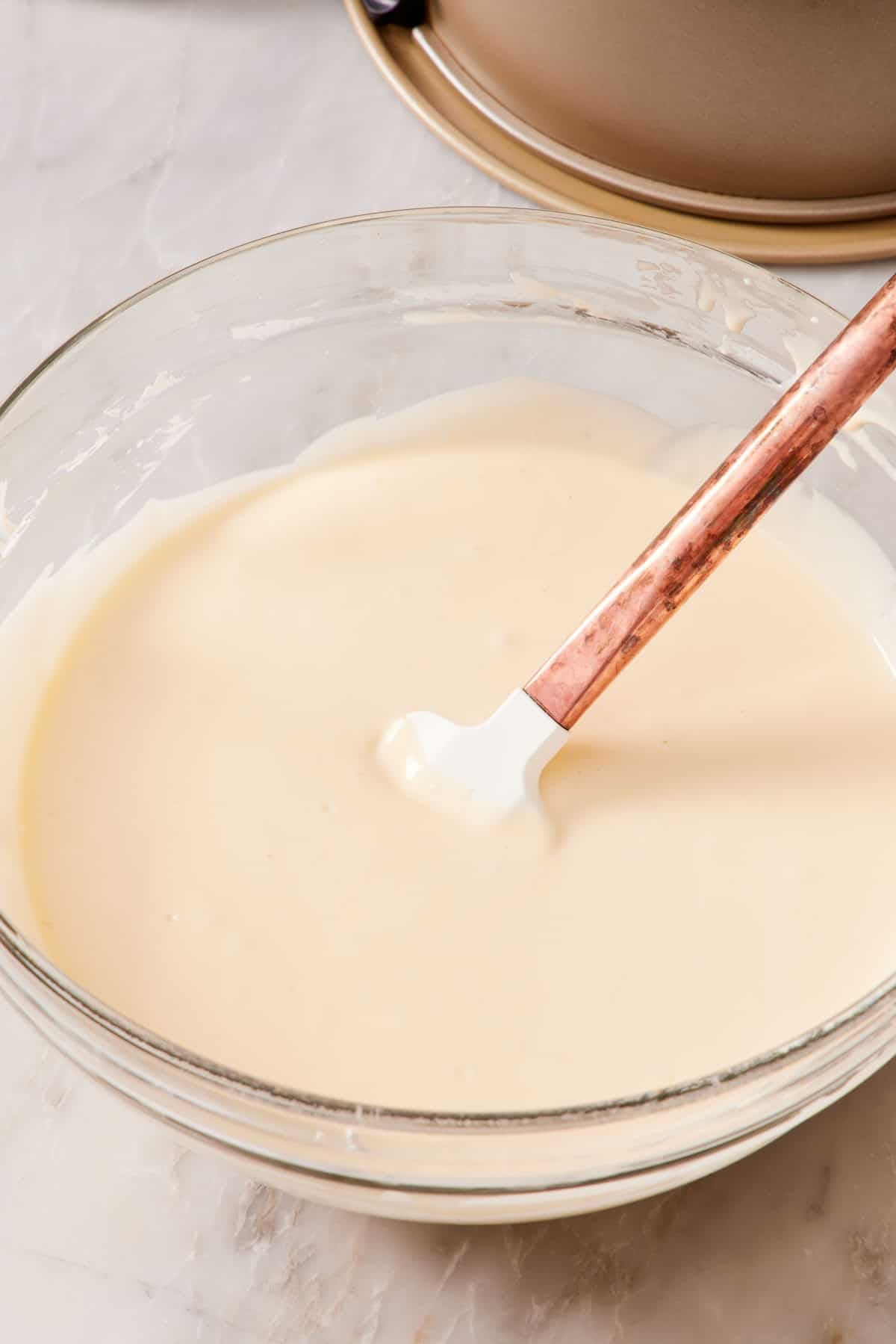 Cheesecake batter in a glass bowl with a spatula.