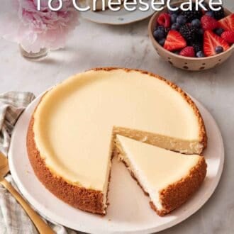 Pinterest graphic showing cheesecake with one slice cut and placed on a plate, and the other slice still with the rest of the cheesecake. A bowl of berries and vase of flowers also in frame.
