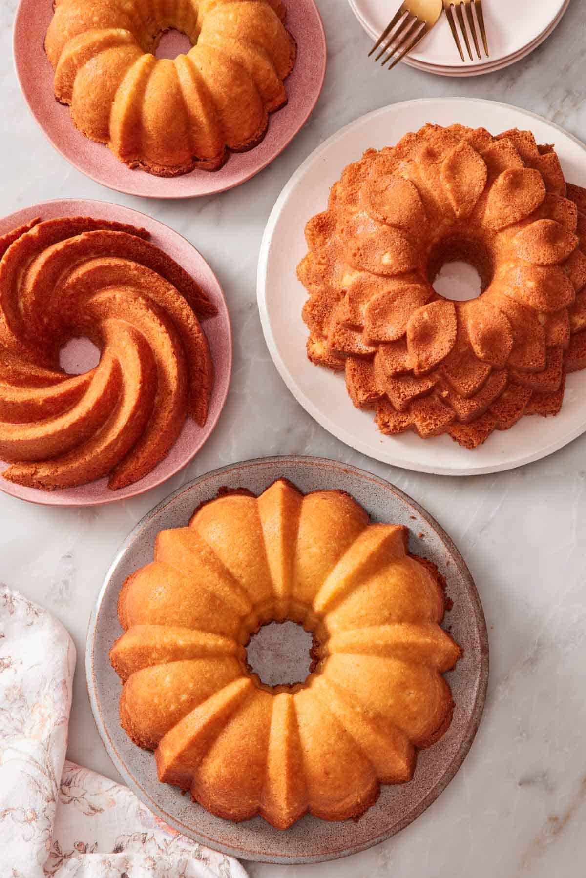 Overhead shot of four bundt cakes on different-sized plates set on a marble countertop.