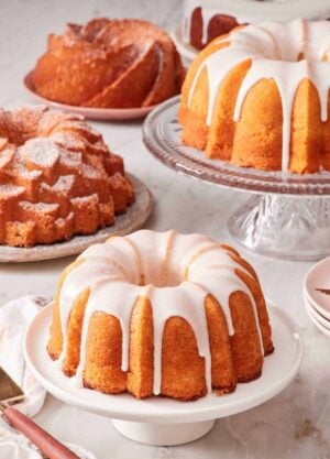 Bundt cakes on cake stands and plates set on a marble countertop.