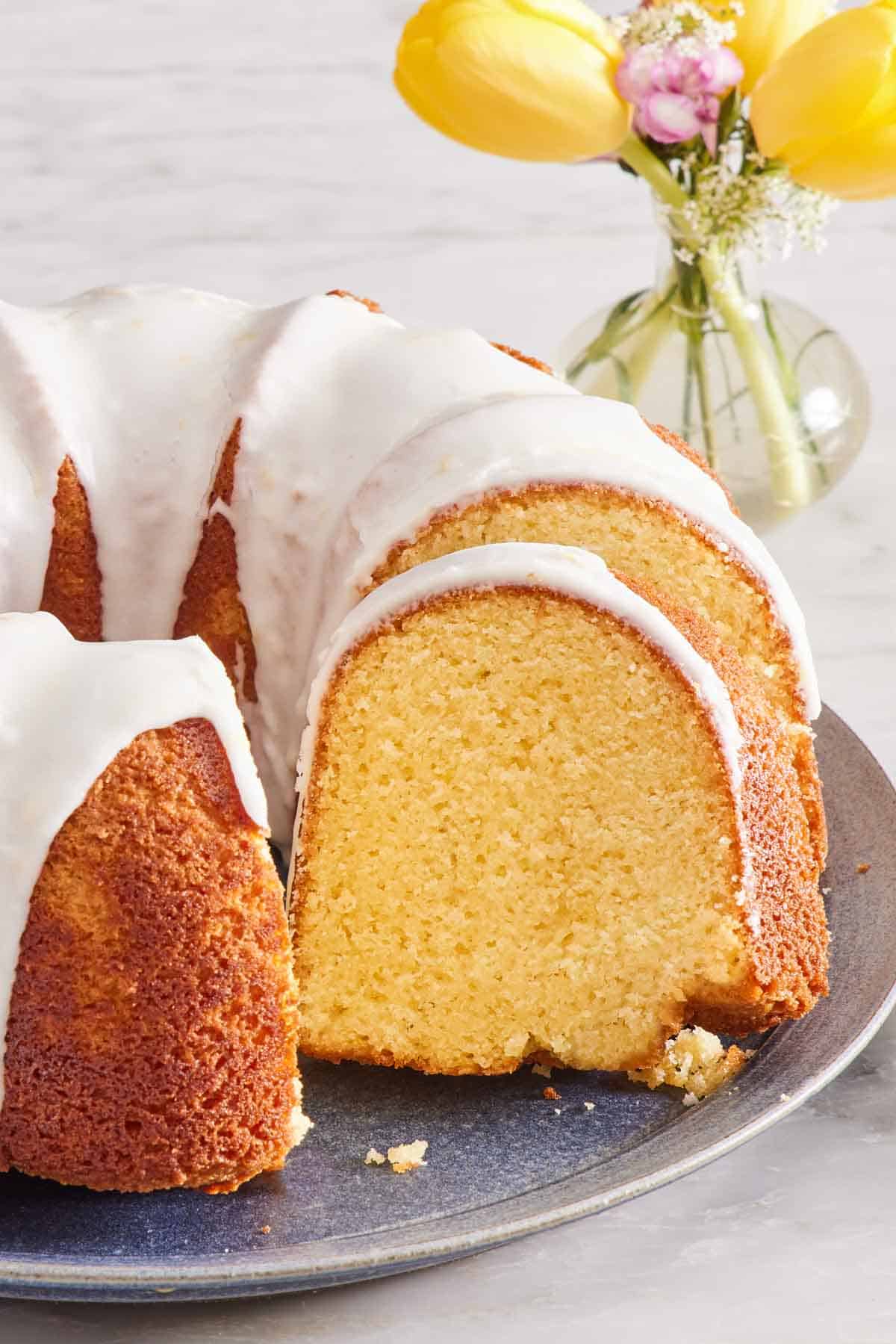 Close-up of lemon Bundt cake with a vase of flowers in the background.