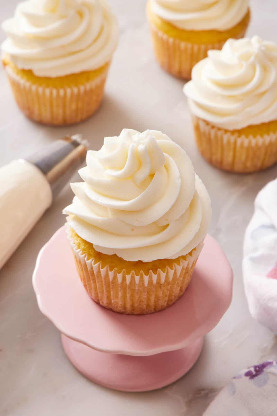 Close-up of a frosted cupcake on a small cake stand with more cupcakes out of focus in the background.