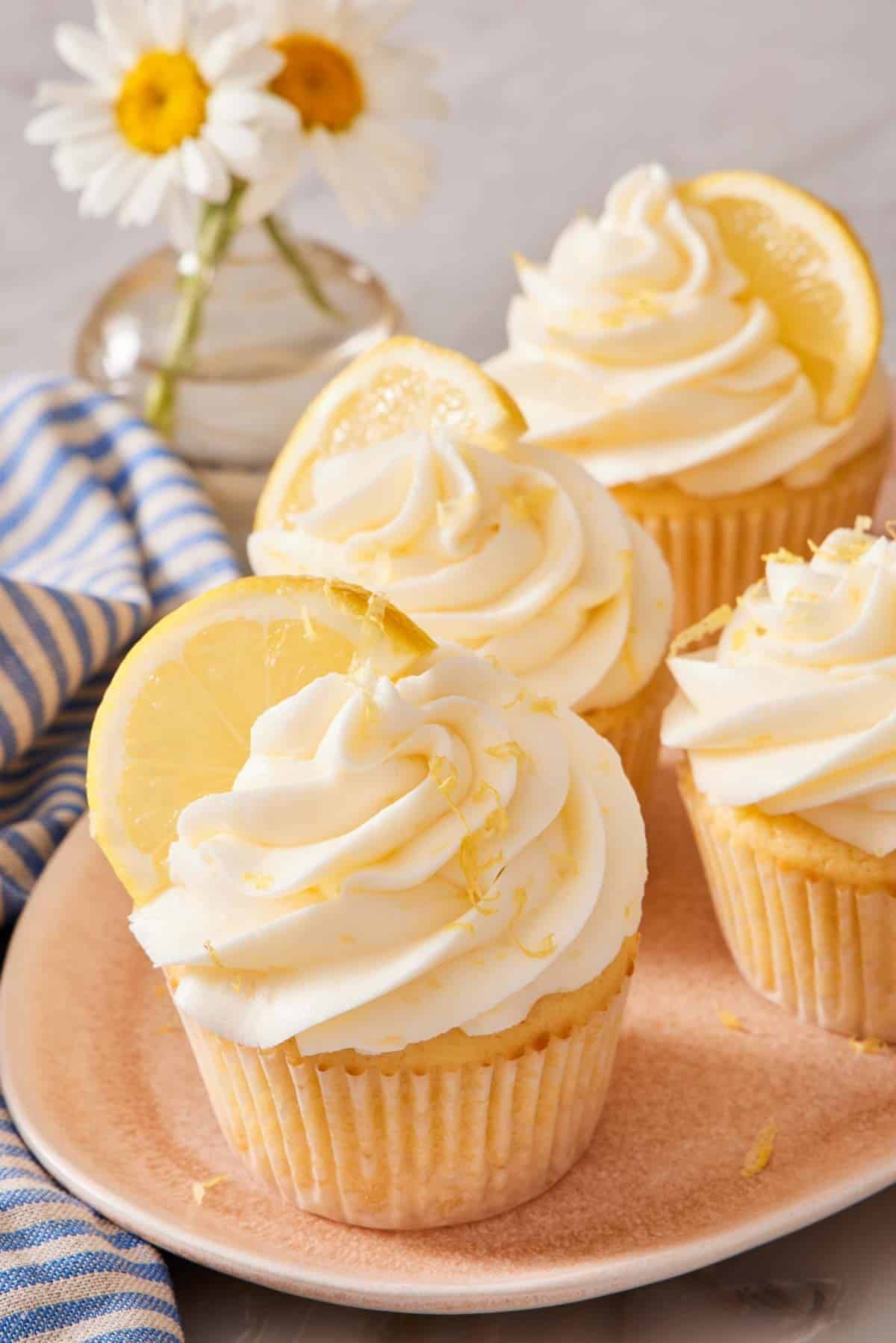 Lemon cupcakes on a platter, garnished with lemon zest and lemon slices.