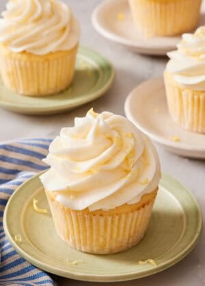 A lemon cupcake on a small plate, with more cupcakes on plates out of focus in the background.