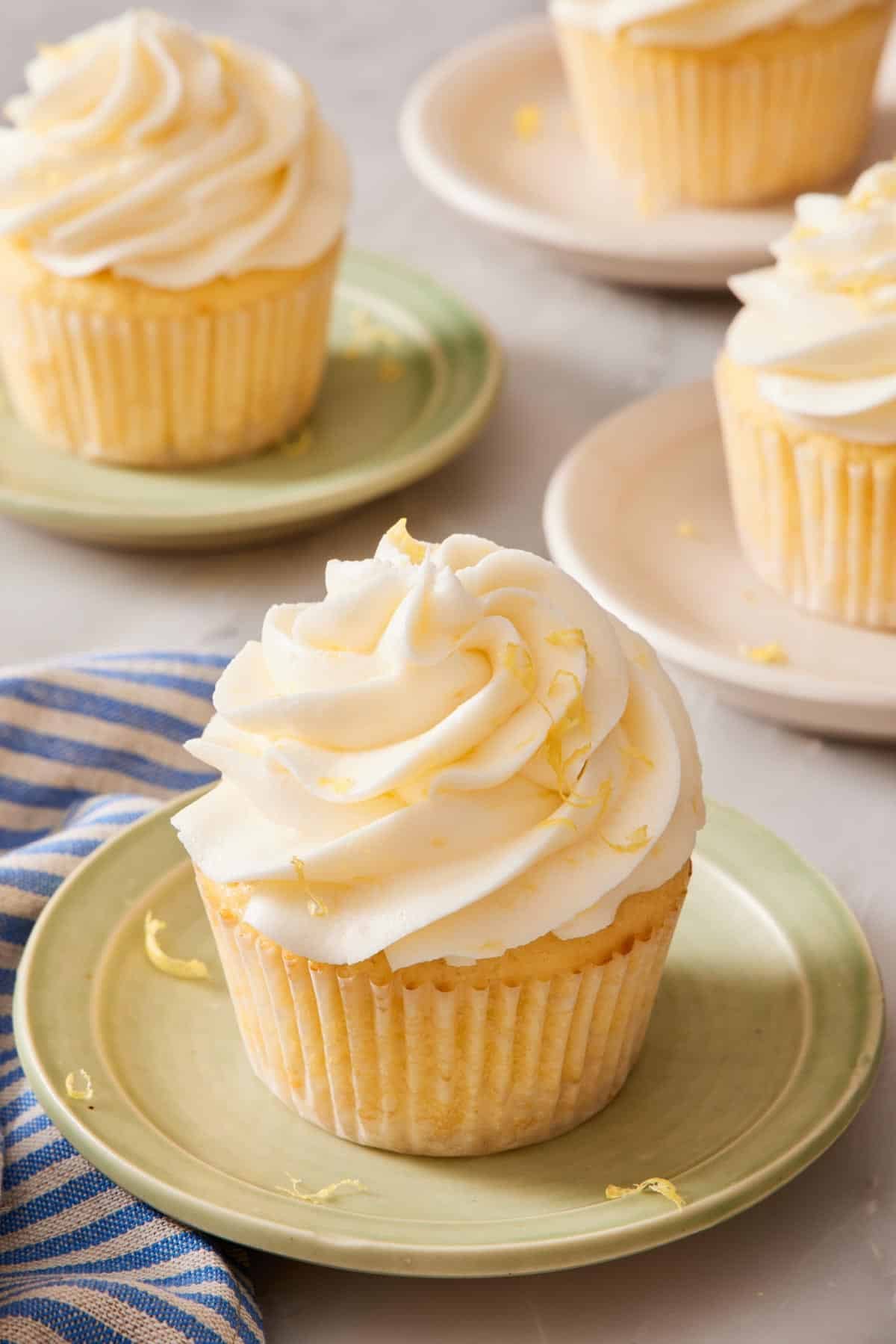 A lemon cupcake on a small plate, with more cupcakes on plates out of focus in the background.