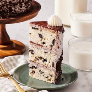A slice of Oreo cake standing up on a plate with two glasses of milk