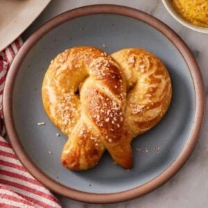 Overhead shot of a soft pretzel on a plate set on a marble countertop, with a striped table linen next to it.