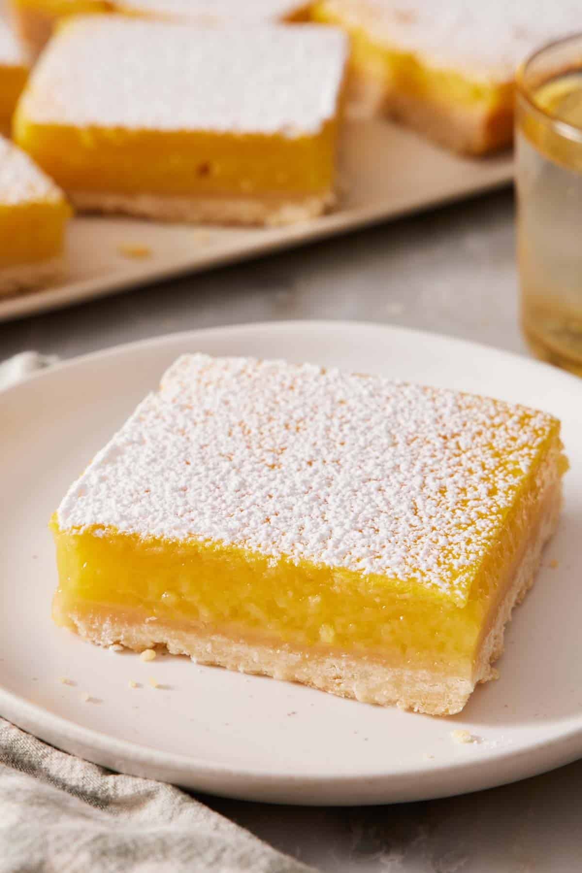 Close-up of a lemon bar on a small plate with more bars out of focus in the background.
