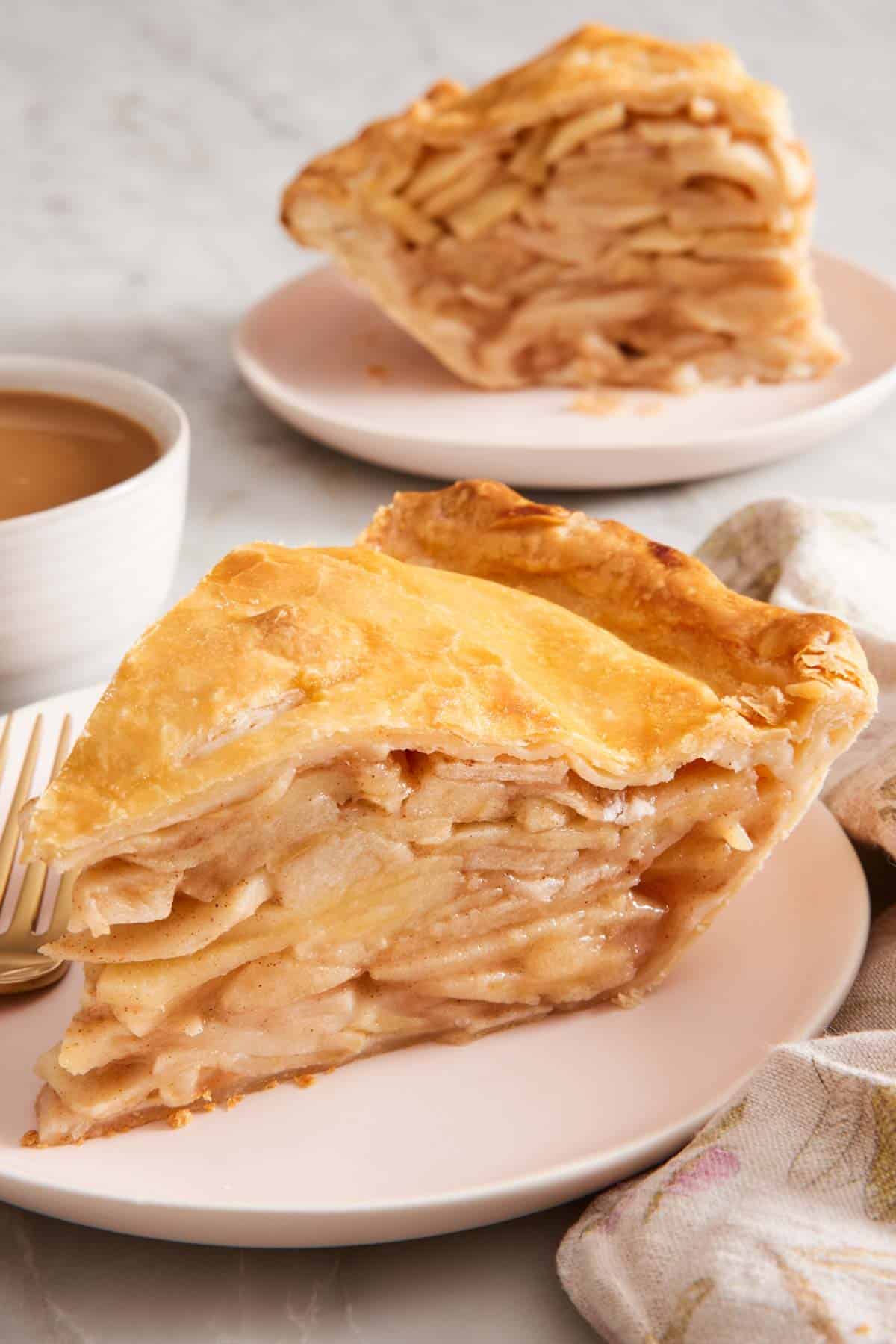 A slice of apple pie on a small plate with another slice in the background.