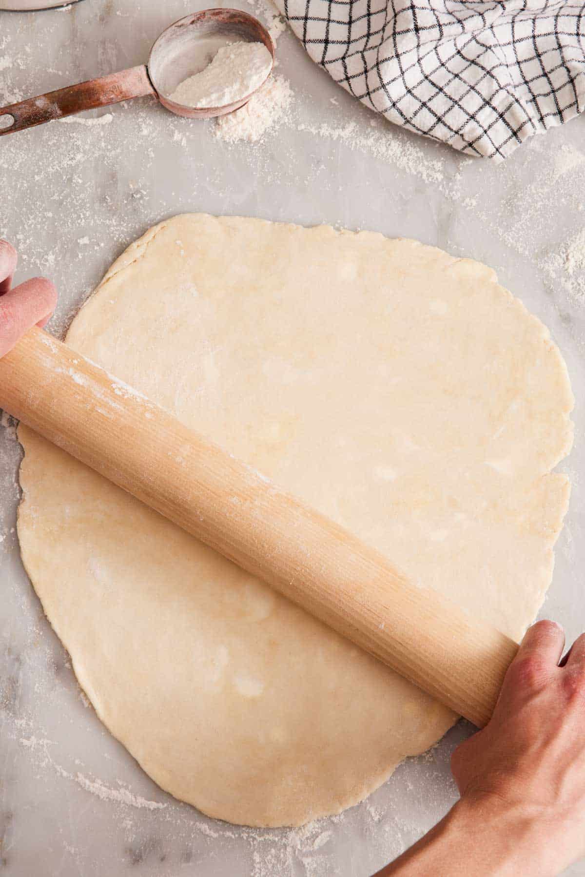 Overhead shot of pie dough being rolled out on a lightly floured countertop.