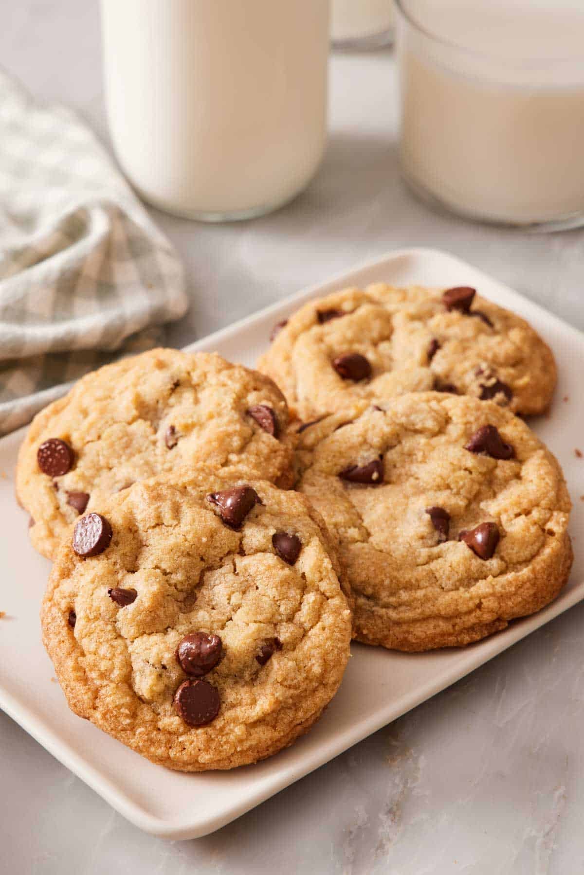 Four cookies on a small plate with glasses of milk in the background.