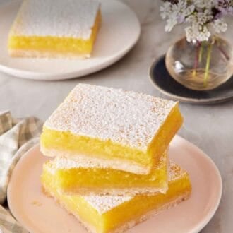 Pinterest graphic showing a stack of three lemon bars on a small plate with another one on a plate in the background.