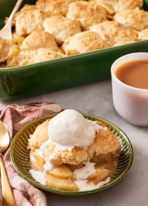Apple cobbler in a bowl with ice cream with the rest of the cobbler in the background.