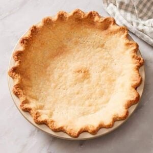 A baked pie crust in a pie dish with a table linen on the side.