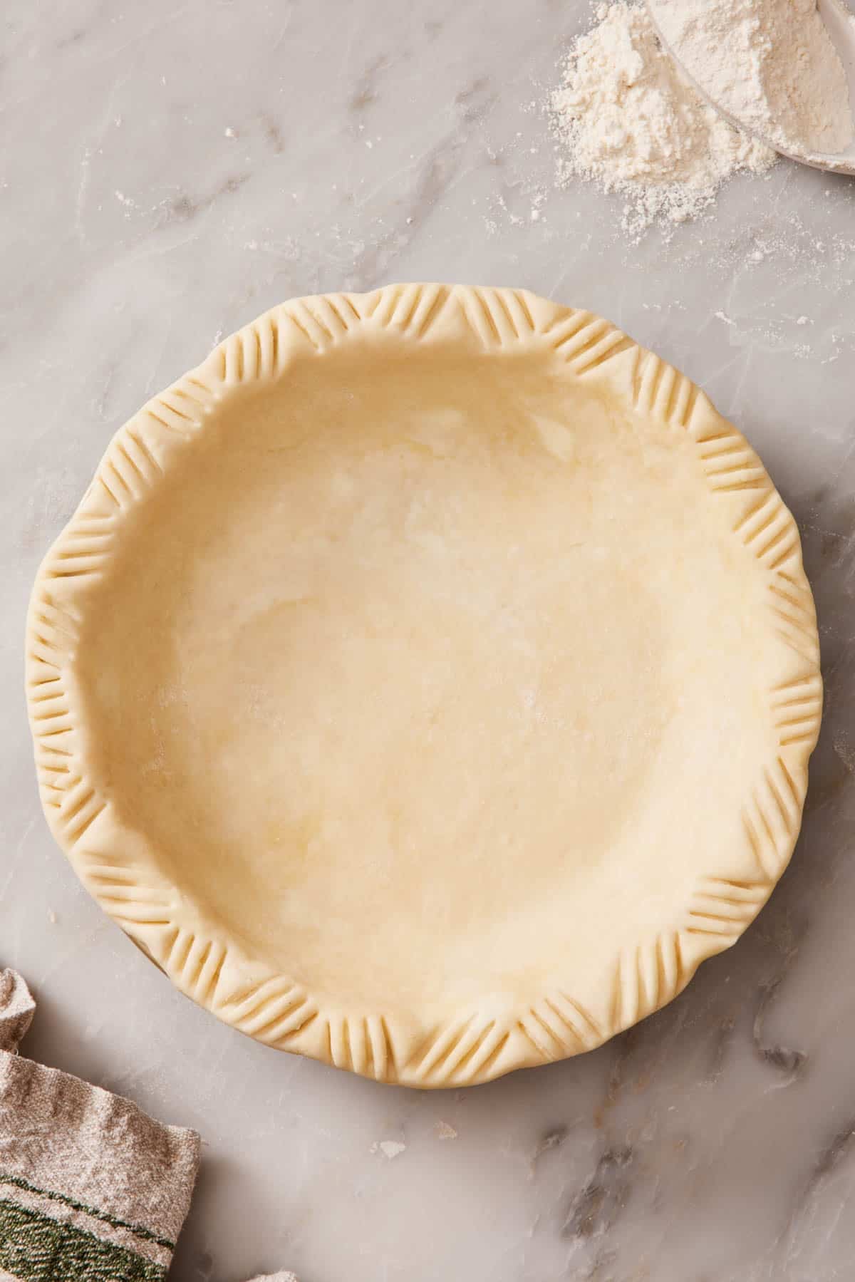 Overhead shot of an unbaked pie crust in a pie dish with fork-decorated edges.