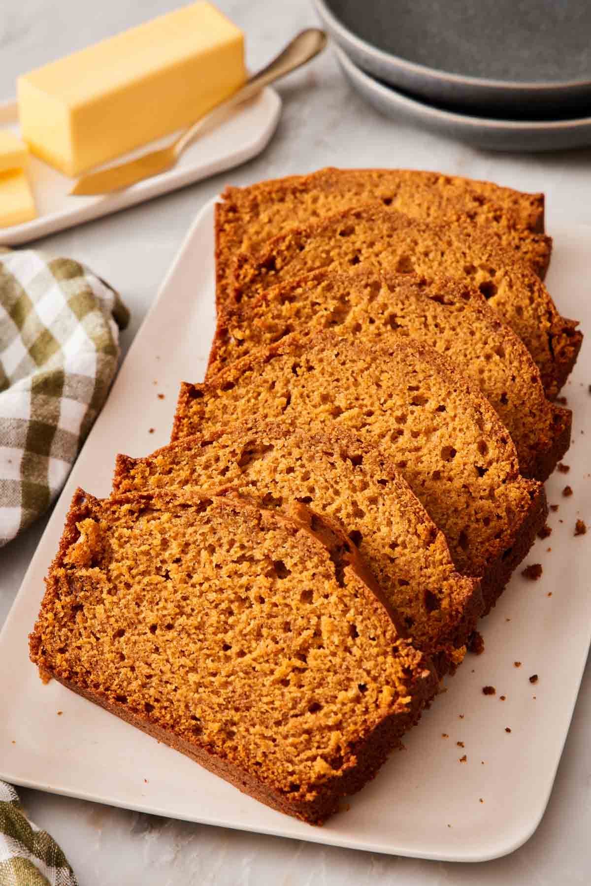Sliced pumpkin bread loaf on a platter with a stick of butter in the background.