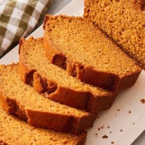 Close-up of mostly sliced loaf of pumpkin bread on a white platter with a table linen on the side.