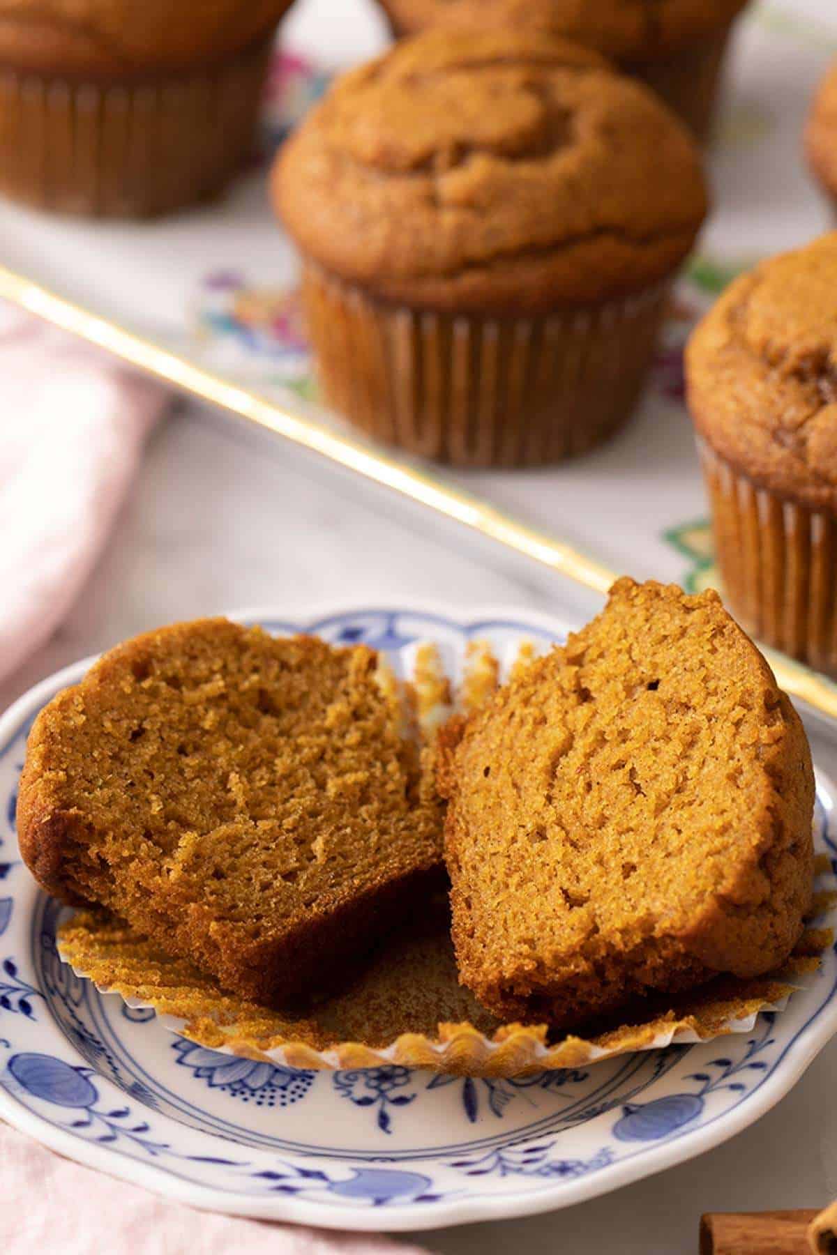 A halved pumpkin muffin on a small plate with more in the background.