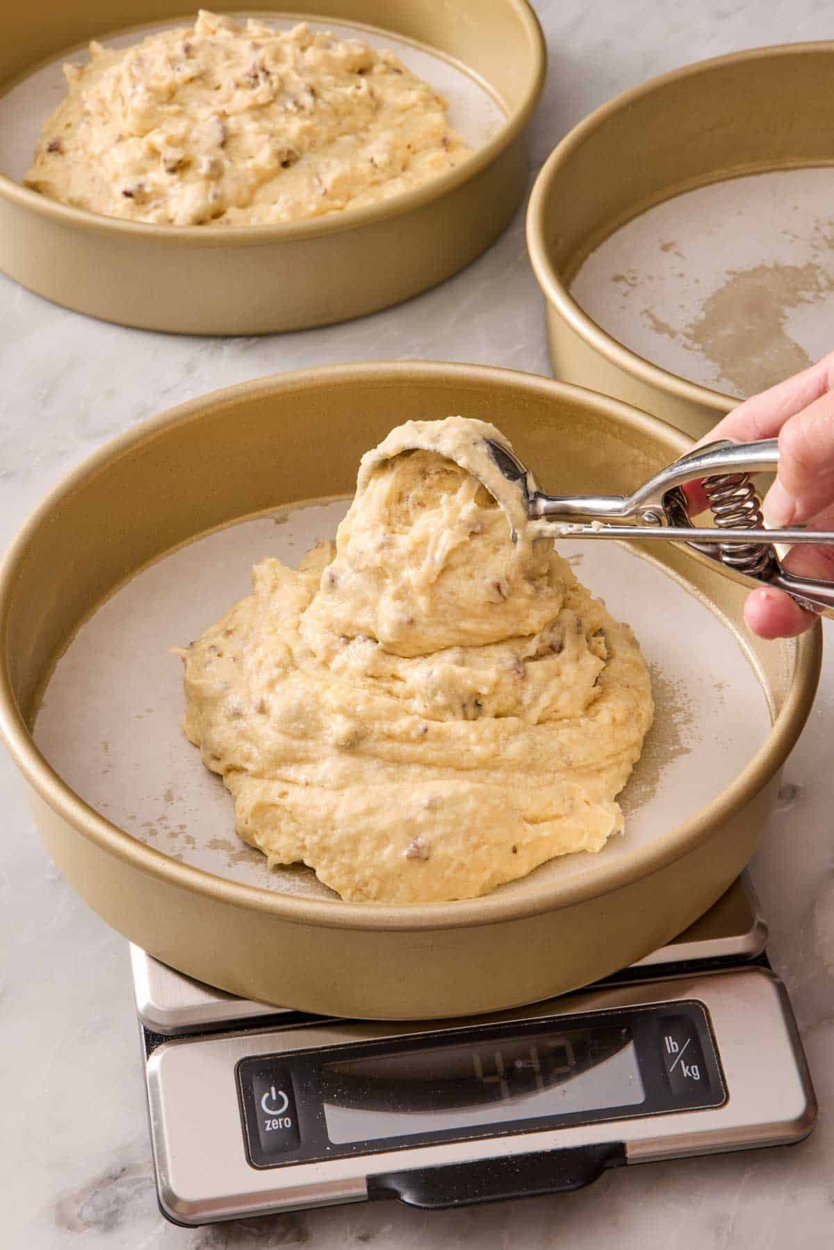 Cake batter scooped into a cake pan, which has been placed on a scale, in order to weigh the batter.