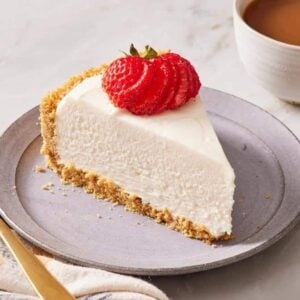 Close-up of a slice of no bake cheesecake with a strawberry on top next to a cup of coffee.