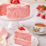 A strawberry cake on a cake stand with a slice cut and placed in front.