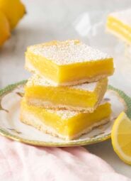 Lemon bars dusted with powdered sugar on a green and white plate.