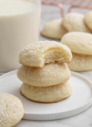 Cream cheese cookies stacked next to a glass of milk.