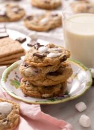 A stack of three s'more cookies on a plate with a glass of milk in the back.