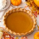 A pumpkin pie next to lots of mini pumpkins and a bowl of whipped cream.